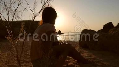 年轻的嬉皮士波霍女孩坐在沙滩上，弹着四弦琴吉他在令人惊叹的日落附近的<strong>海洋</strong>。 <strong>高清</strong>慢镜头。